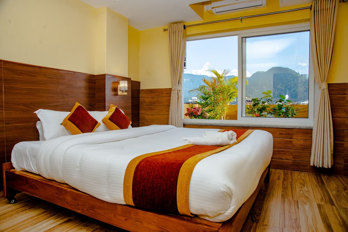 A hotel room with a large bed, wooden headboard, and a view of mountains through the window.