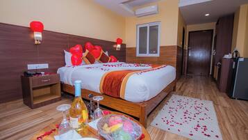 Habitación de hotel con cama, mesita de noche y una pequeña mesa con una botella, copa de vino y un frutero.