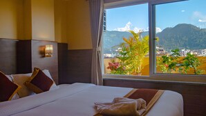A hotel room with a large bed, a view of mountains, and a window with curtains. - Hotel Hidden Kingdom (Pokhara)