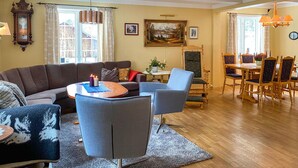 Un salon comprenant un canapé, des fauteuils, une table à manger avec des chaises, une horloge et un tableau accroché au mur.