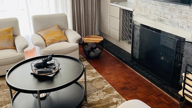 A modern living room with a fireplace, two sofas with cushions, a coffee table, and a TV mounted above the fireplace. - Immaculate Home in Avondale West - 2166 (Harare)