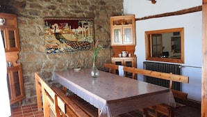 Ein rustikaler Essbereich mit Steinwand, Holzbanken, einem langen Tisch und einer hängenden Leuchte.