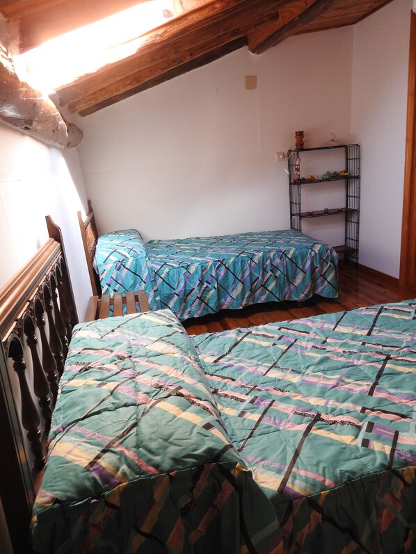 A room with two beds, wooden headboards, a metal shelf unit, and a sloped ceiling.