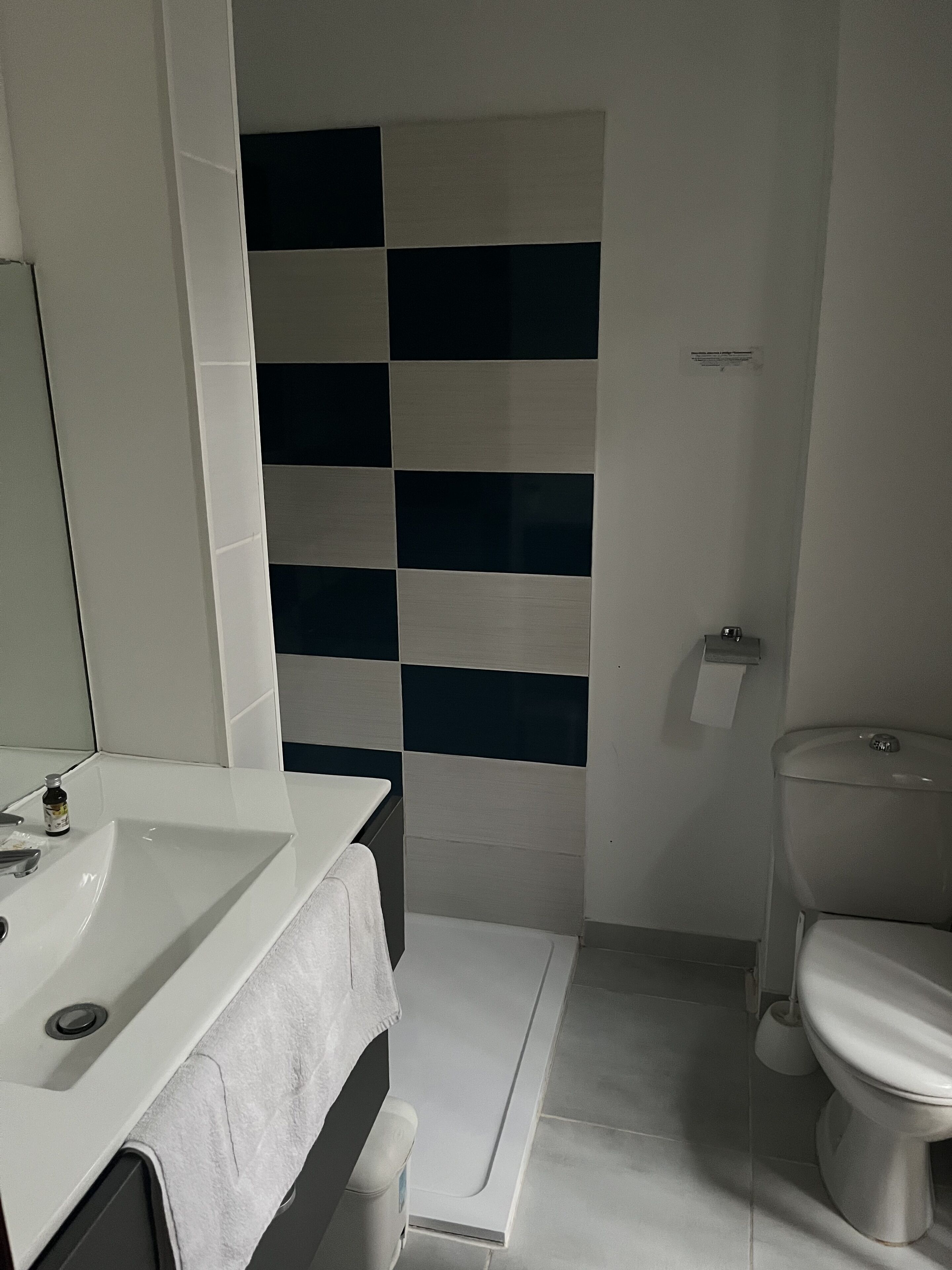 A bathroom with a white sink, a towel, a toilet, and a wall with a checkered pattern.