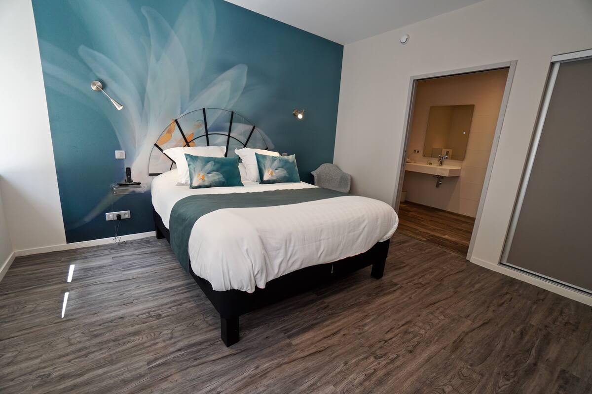A modern bedroom with a large bed, a wall mural, and a bathroom visible through an open door.