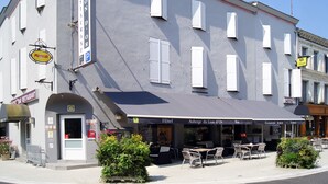 A hotel with a grey facade, outdoor seating area, and multiple signs indicating services like a bar and restaurant.