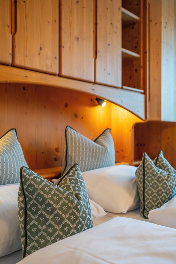 Interior de una cabaña de madera con una cama, almohadas y una estantería.