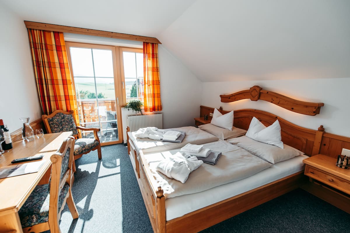 A hotel room with a wooden bed, a desk, and a chair. There is a window with curtains and a view of the outdoors.