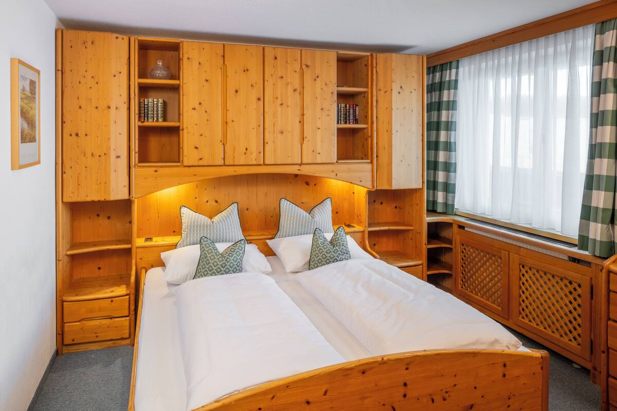 A wooden bedroom with a bed, shelves, and a window with curtains.