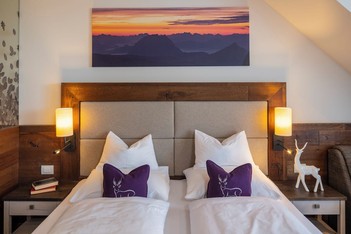 A double bed with white and purple pillows, a wooden headboard, and two bedside lamps.