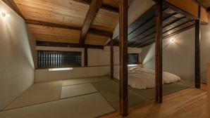 A traditional Japanese room with tatami flooring, a low ceiling with exposed beams, and a bed with white bedding.