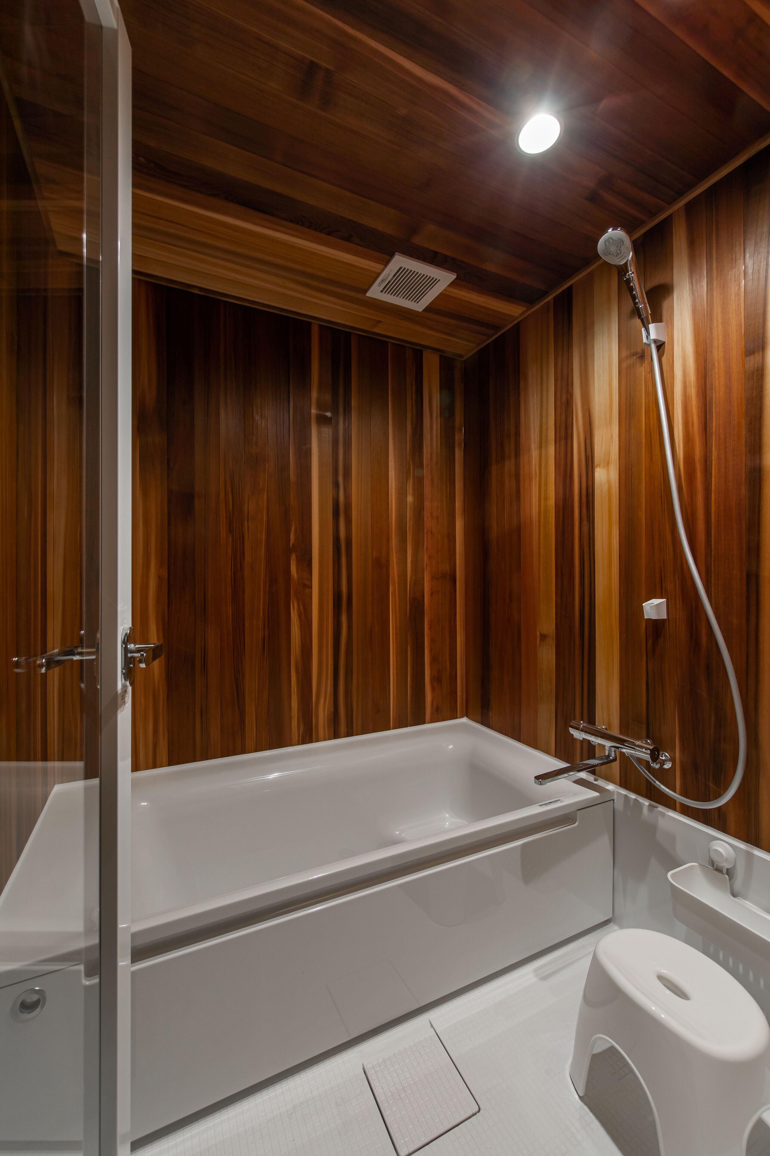 Ein modernes Badezimmer mit einer Wandverkleidung aus Holz, einer weißen Badewanne, einem WC und einer Dusche mit Duschbrause.