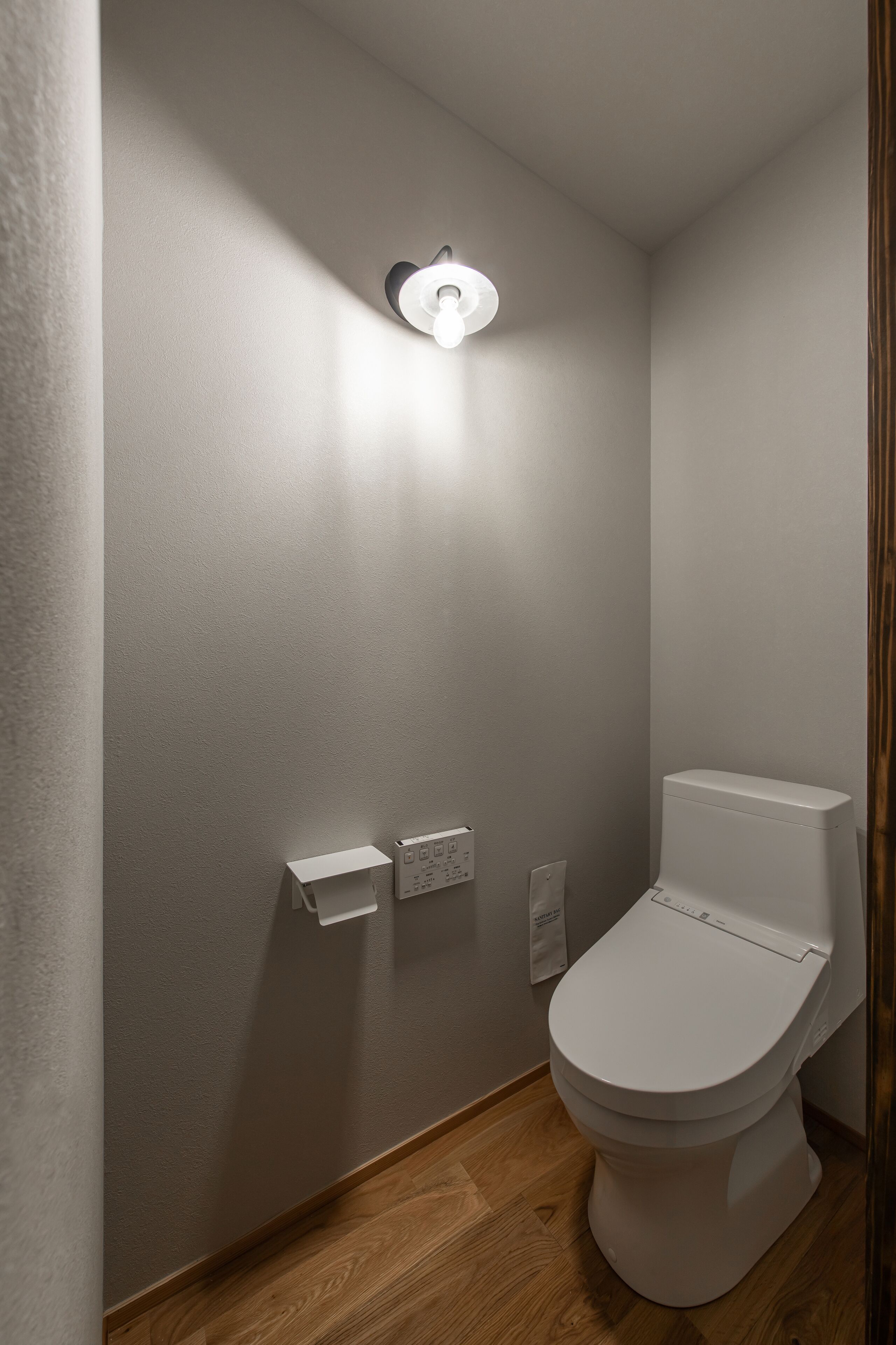 A small, modern bathroom with a toilet, a wall-mounted light, and a toilet paper holder.