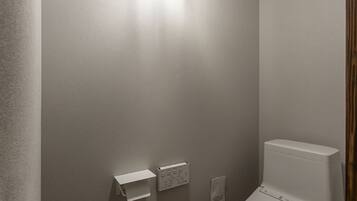 A small, modern bathroom with a toilet, a wall-mounted light, and a toilet paper holder.