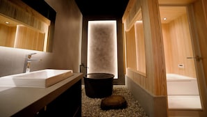 A modern bathroom with a large mirror, a white sink, a black bathtub, and a wooden floor.