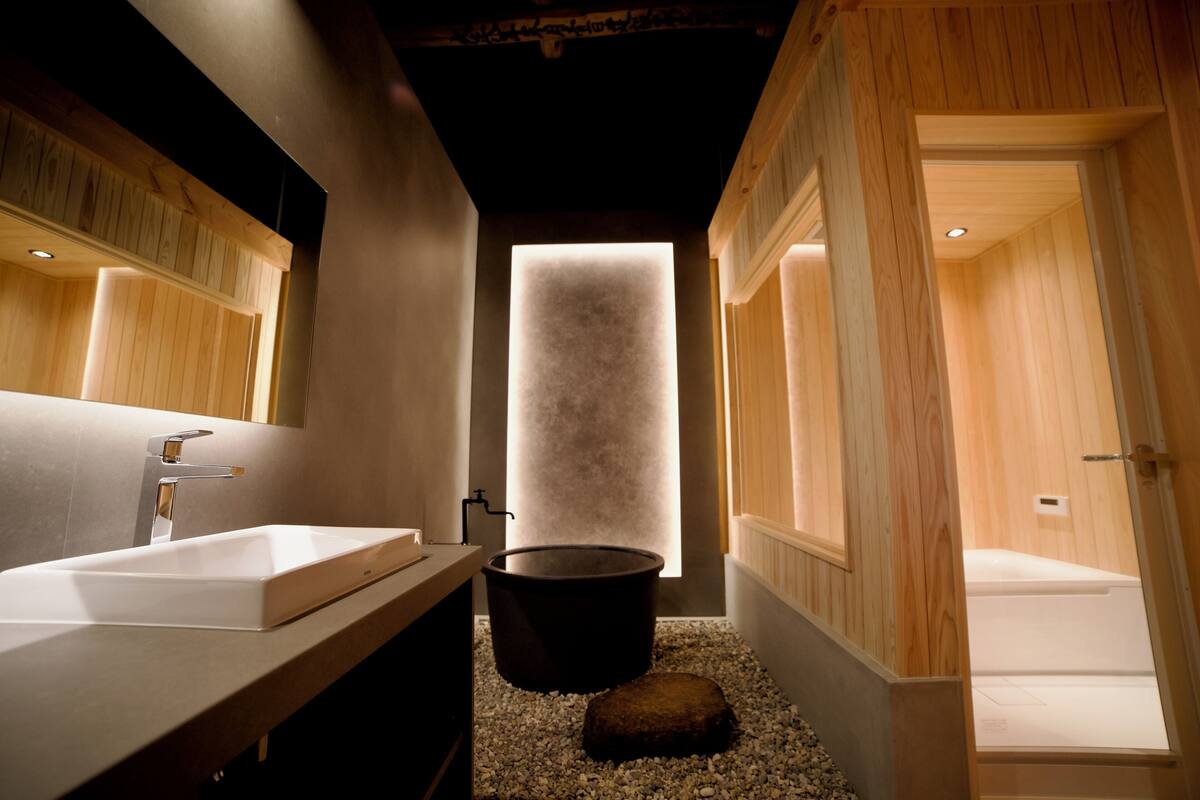Ein modernes Badezimmer mit einem großen Spiegel, einem weißen Waschbecken, einer schwarzen Badewanne und Holzboden.