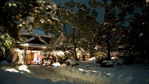 A traditional Japanese building with a snow-covered roof and surrounding trees.