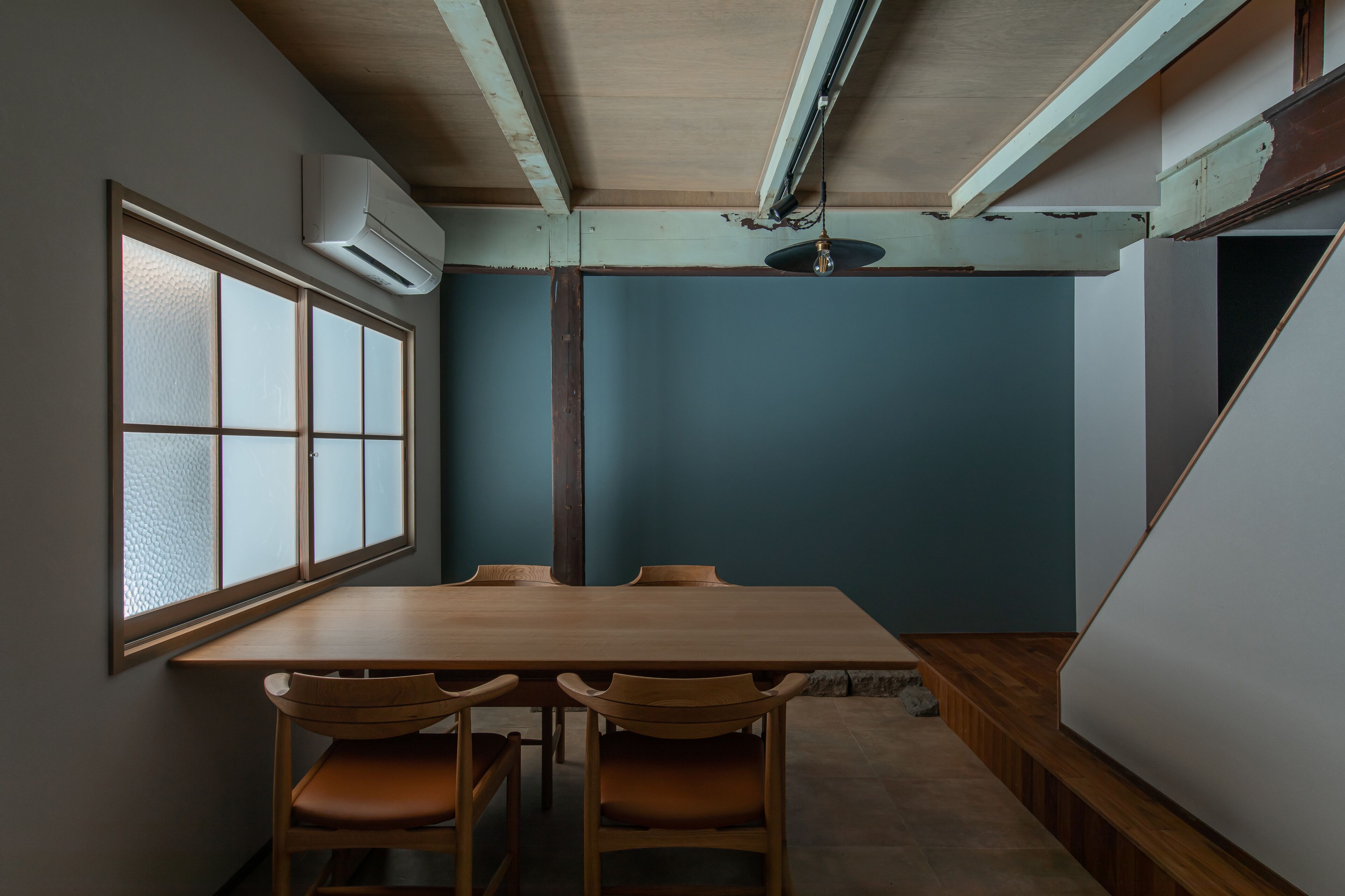 Una habitación con una mesa y sillas de madera, un ventanal con vidrio esmerilado y una pared de acento azul.