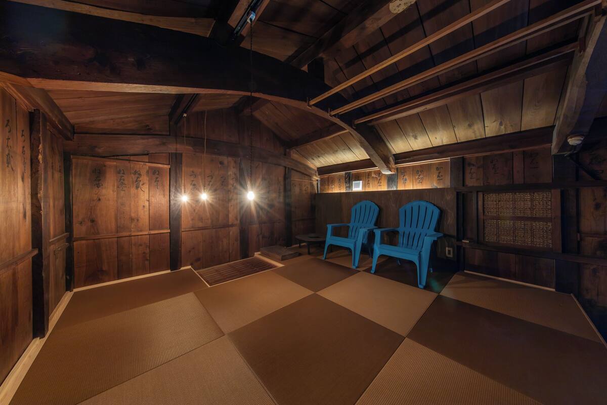 Ein Raum mit Tatami-Matten, Holzwänden, zwei blauen Stühlen und einem kleinen Tisch.