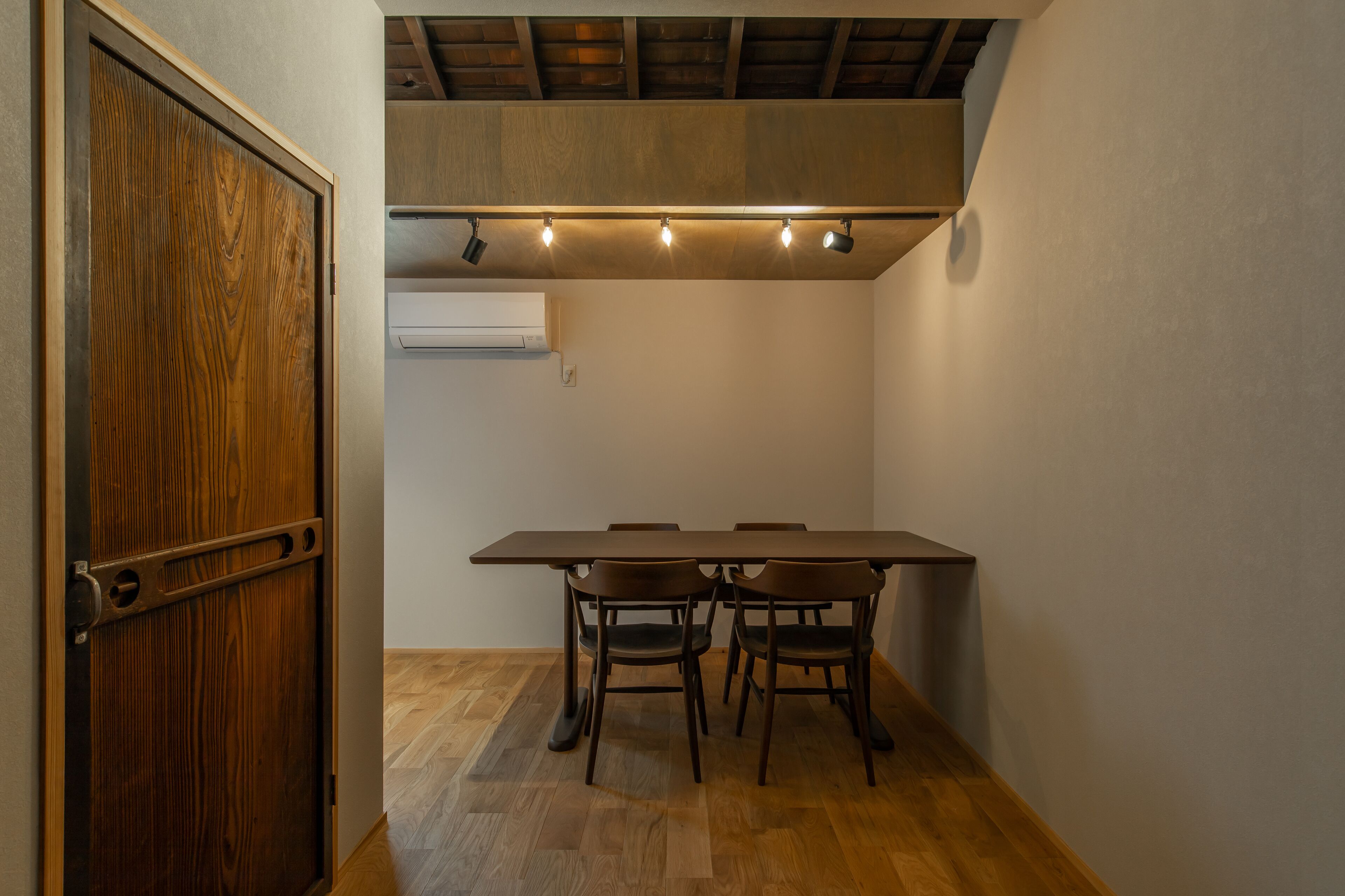 A room with a wooden door, a table with four chairs, and a ceiling light fixture.