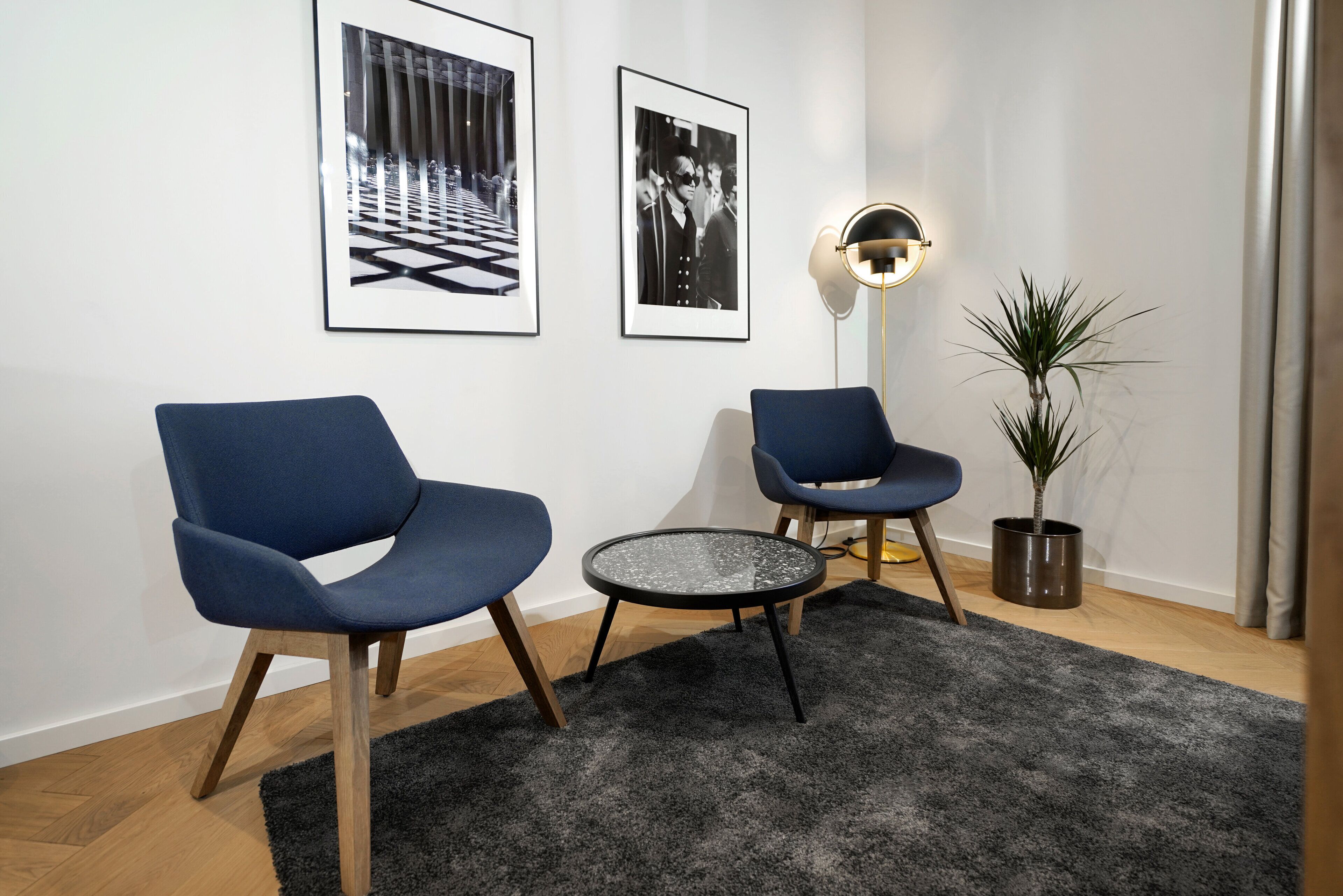 A modern living room with two blue armchairs, a small round table, a floor lamp, and a potted plant.