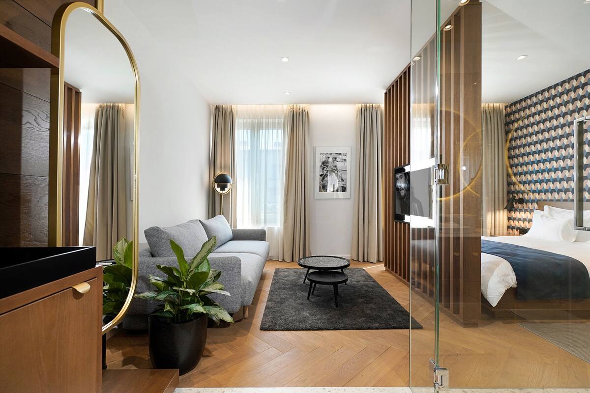 A modern hotel room with a sofa, a bed, a small round table, and a large mirror.