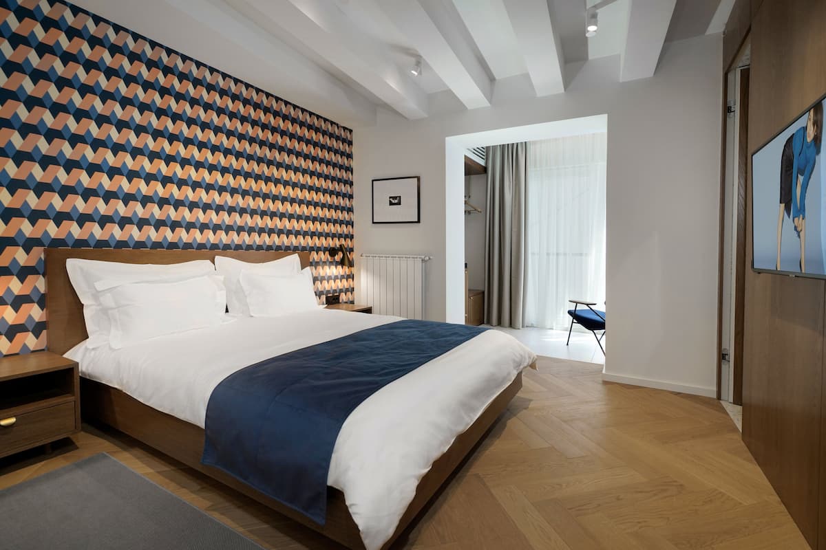 A modern bedroom with a patterned wall, a large bed, a radiator, and a view of a balcony.