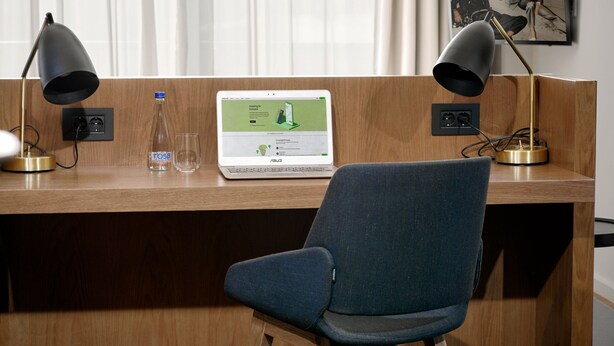 A wooden desk with a laptop, two lamps, a water bottle, and a framed picture on the wall. - Dominic Smart & Luxury Suites - Edition (Belgrade)