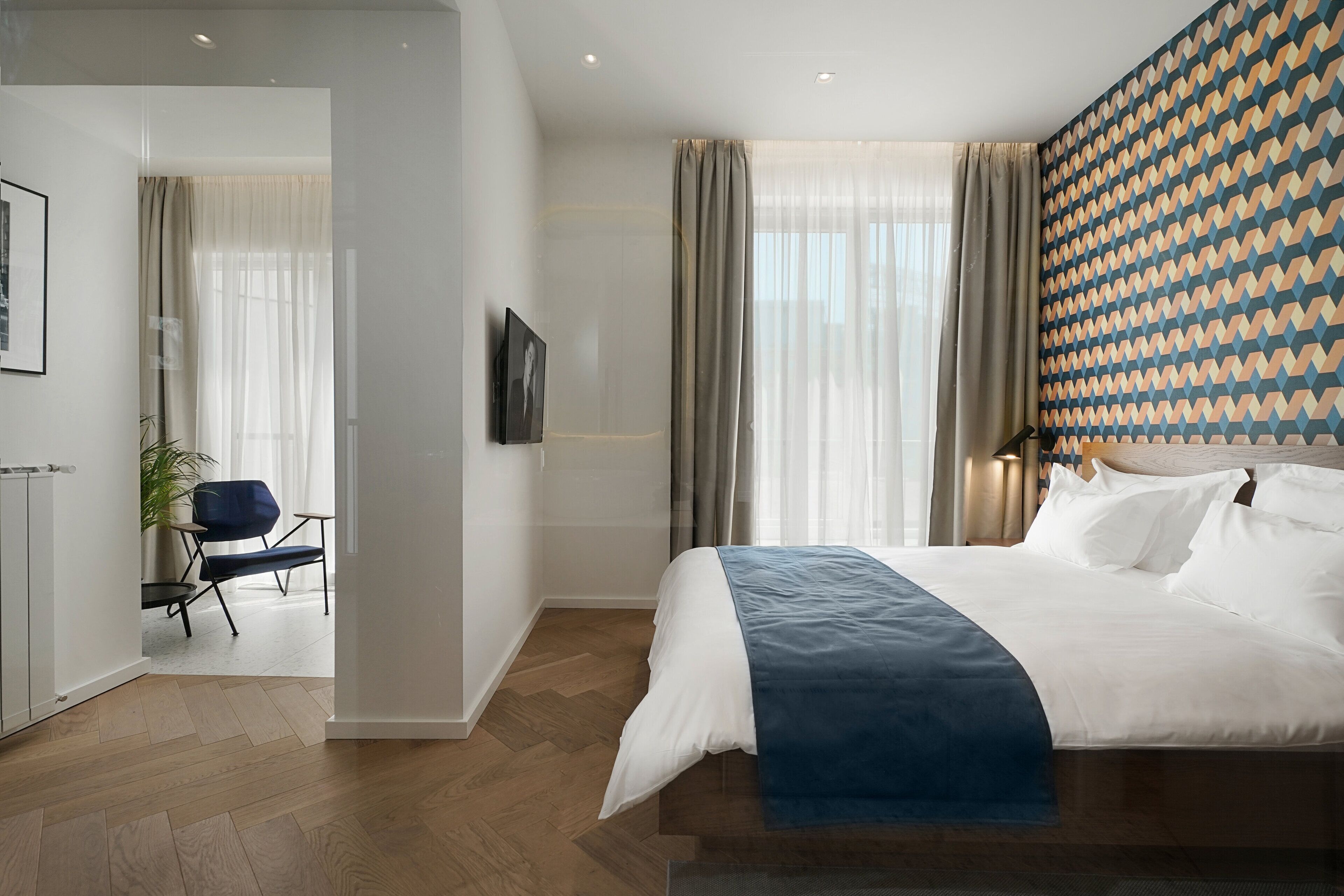 A modern hotel room with a large bed, a blue accent, a patterned wall, and a view of the hallway.