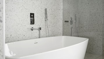 A modern bathroom with a freestanding bathtub, a handheld showerhead, and a wall-mounted faucet.