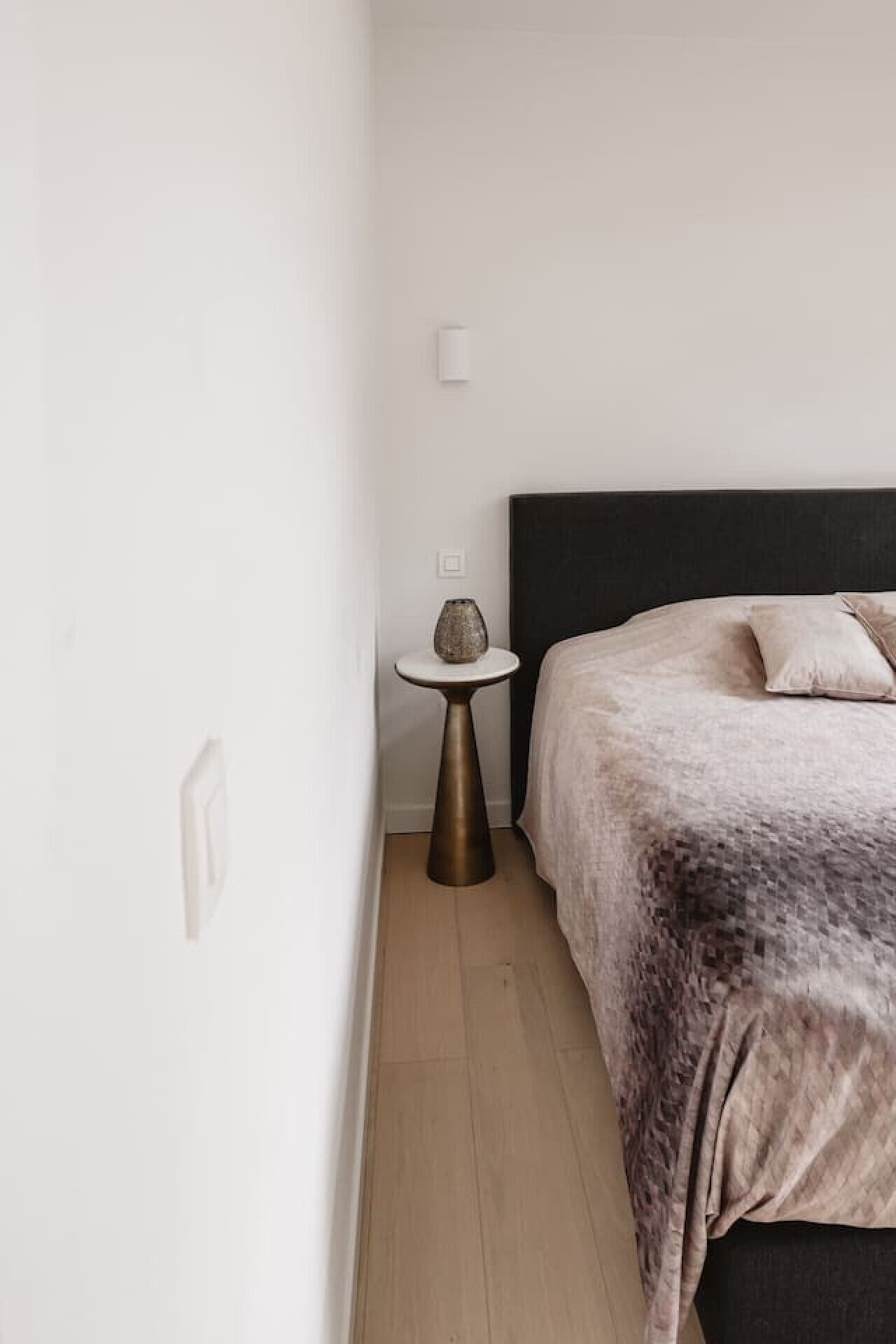 A bedroom with a bed, a bedside table, and a wall-mounted light.