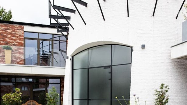 En moderne bygning med en buet glasfacade, en spiraltrappe og plantekasser i gården.
