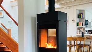En moderne stue med en sort brændeovn, en trappe og et spiseområde.