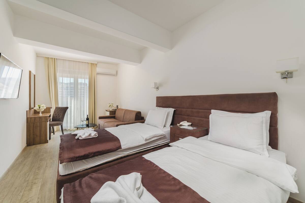 A hotel room with two beds, a desk, a chair, a small table, and a window with curtains.