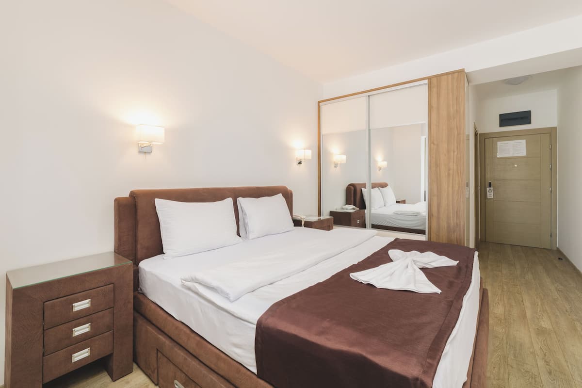 A hotel room with a large bed, a wooden nightstand, a mirror, and a wardrobe.