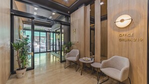 Ein modernes Bürointerieur mit Empfangsbereich, inklusive Empfangstresen, zwei Stühlen, einem kleinen Tisch und einer Topfpflanze.