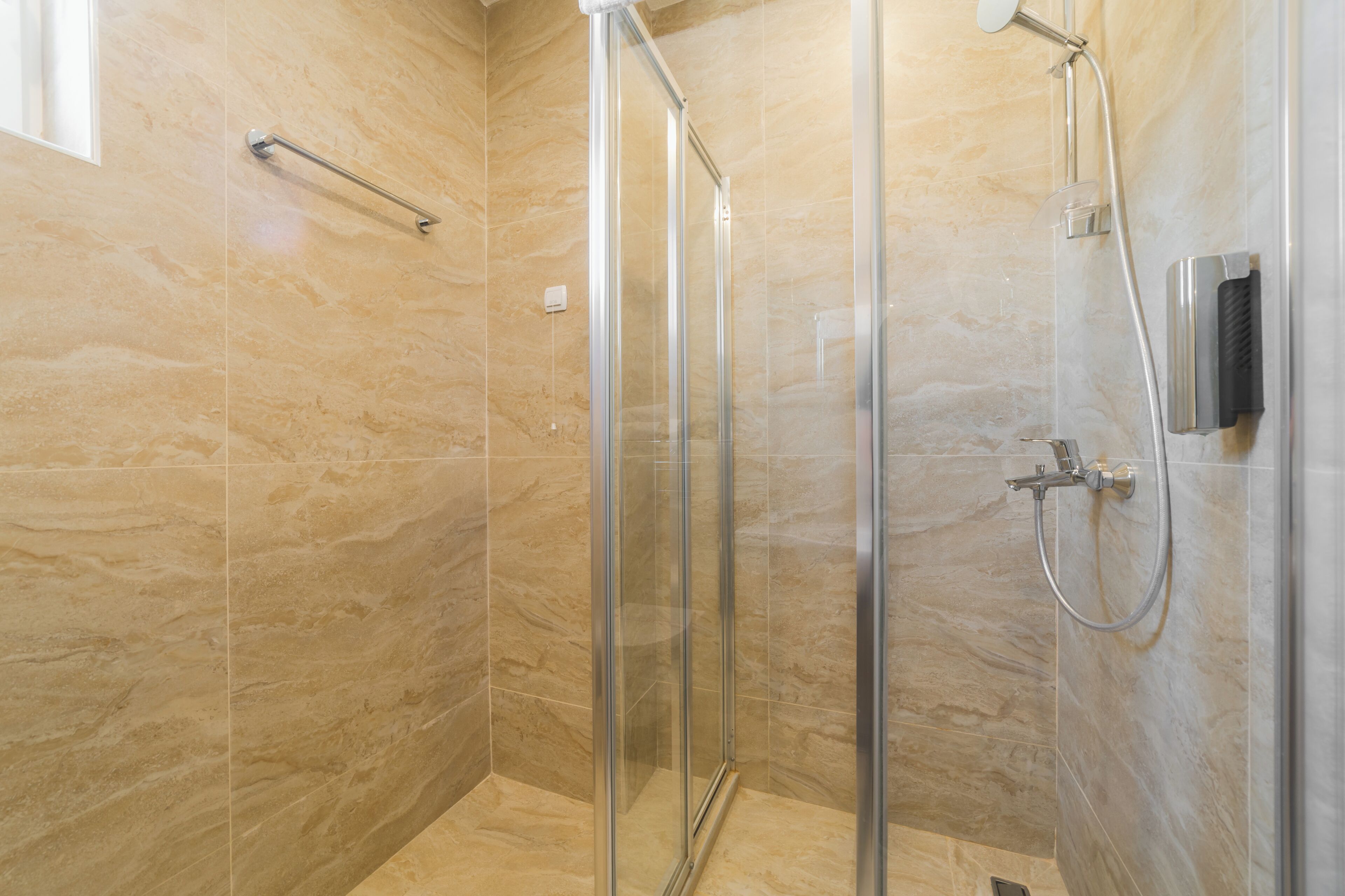 Una ducha moderna con puerta de vidrio, cabezal de ducha de mano y panel de control en la pared.