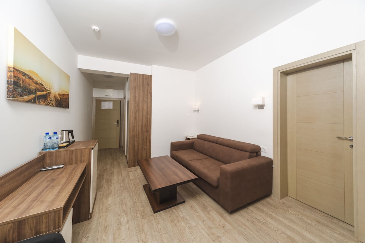 A modern hotel room with a wooden desk, a brown sofa, a wooden coffee table, and a painting on the wall.