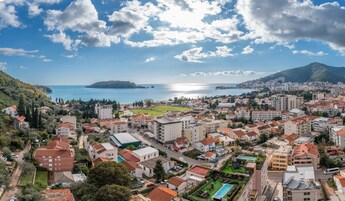 Un pueblo costero con una mezcla de edificios residenciales y comerciales, una vista despejada del mar y un paisaje montañoso de fondo.
