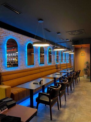 A restaurant with brick walls, neon signs, and a long counter with seating. - Hotel 219 Budva (Budva)