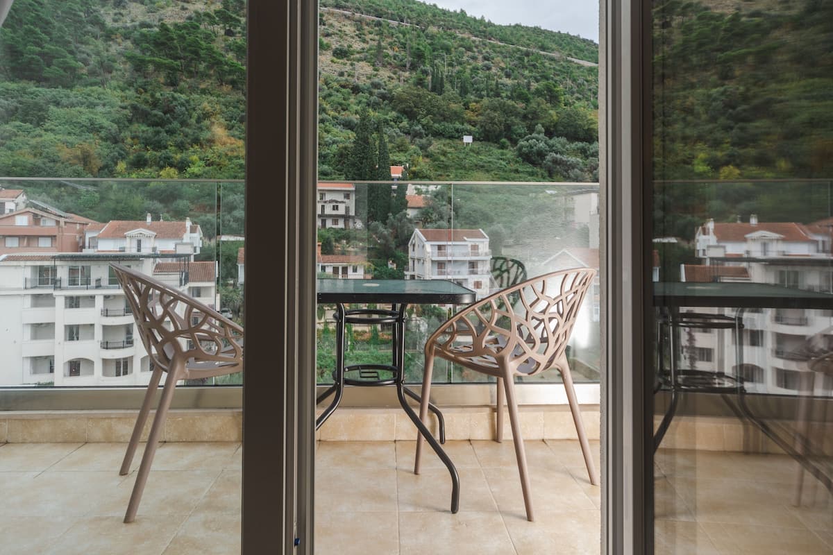 A balcony with two chairs and a table, overlooking a hillside with buildings.