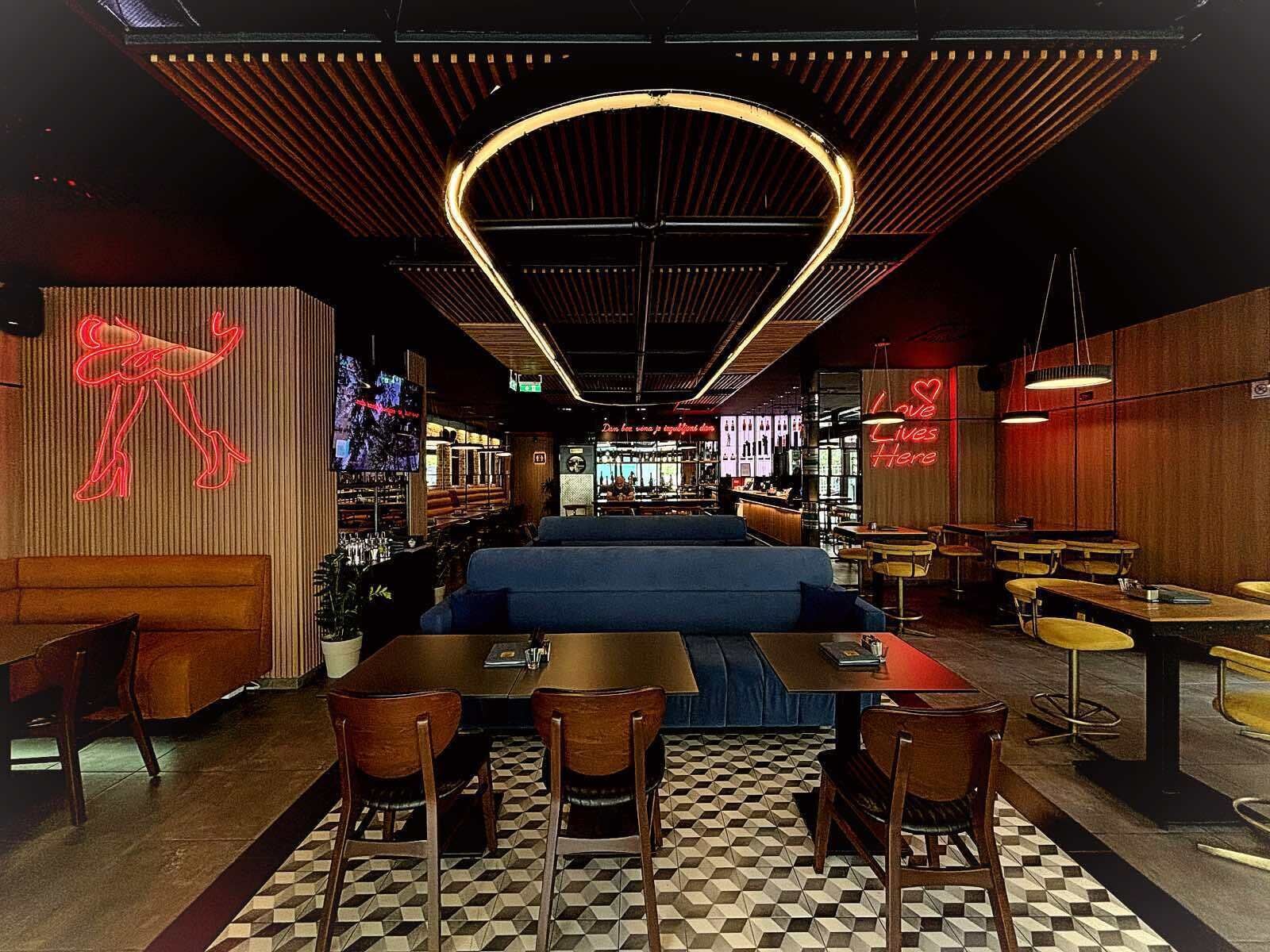 A modern restaurant interior with a bar area, seating arrangements, and a neon sign.
