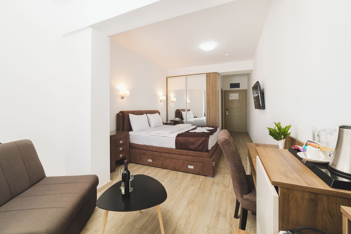 Una habitación de hotel moderna con cama, escritorio, silla, una mesita con una botella y una planta en maceta.