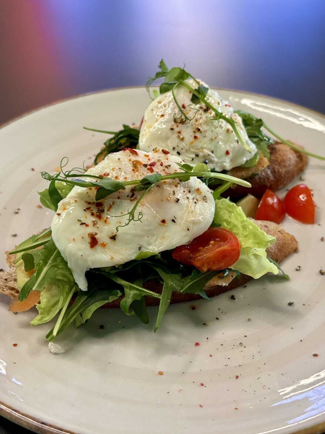 A plate with a salad, poached eggs, and cherry tomatoes.