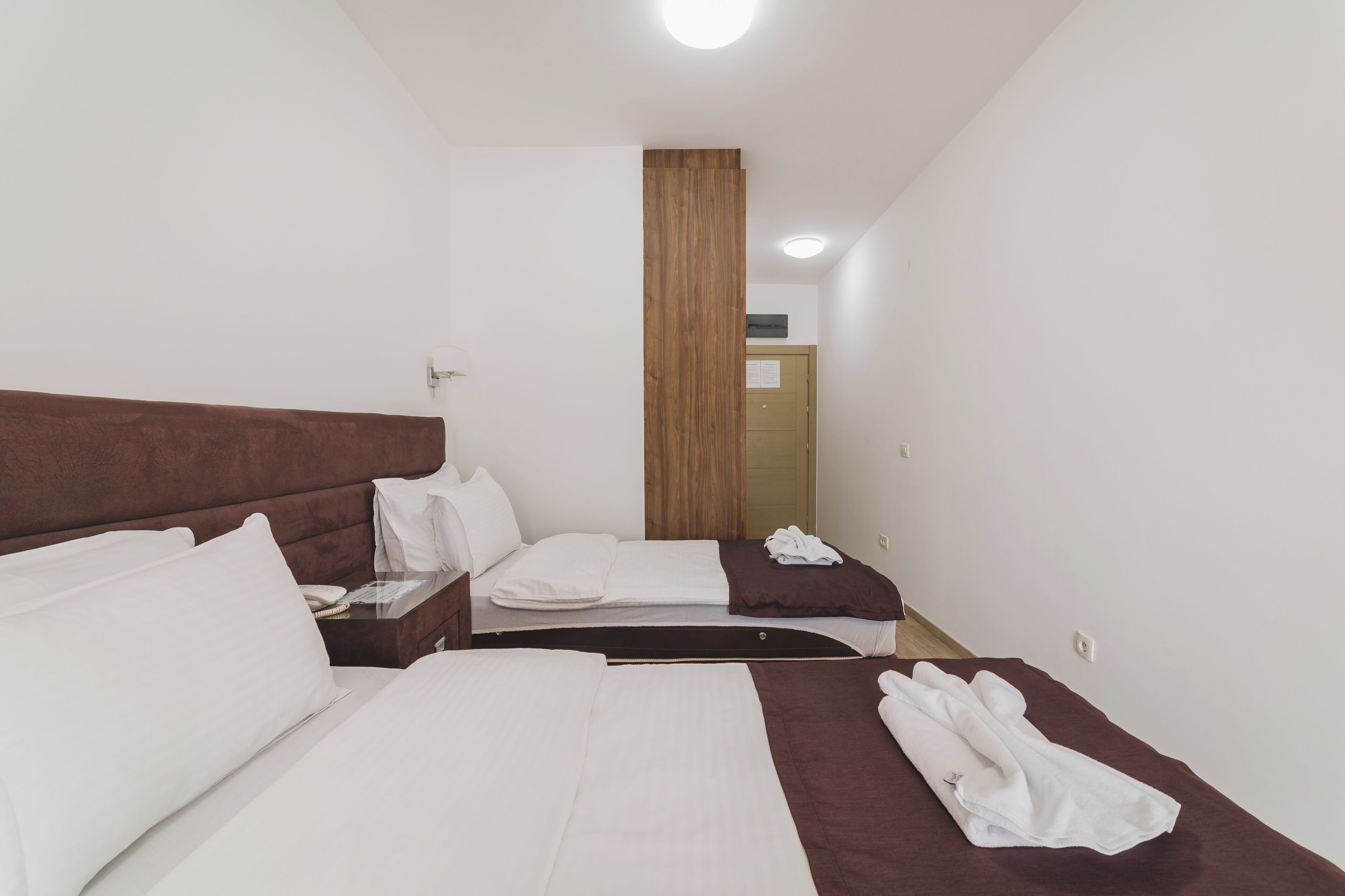 A hotel room with two beds, a wooden accent wall, and a visible door in the background.