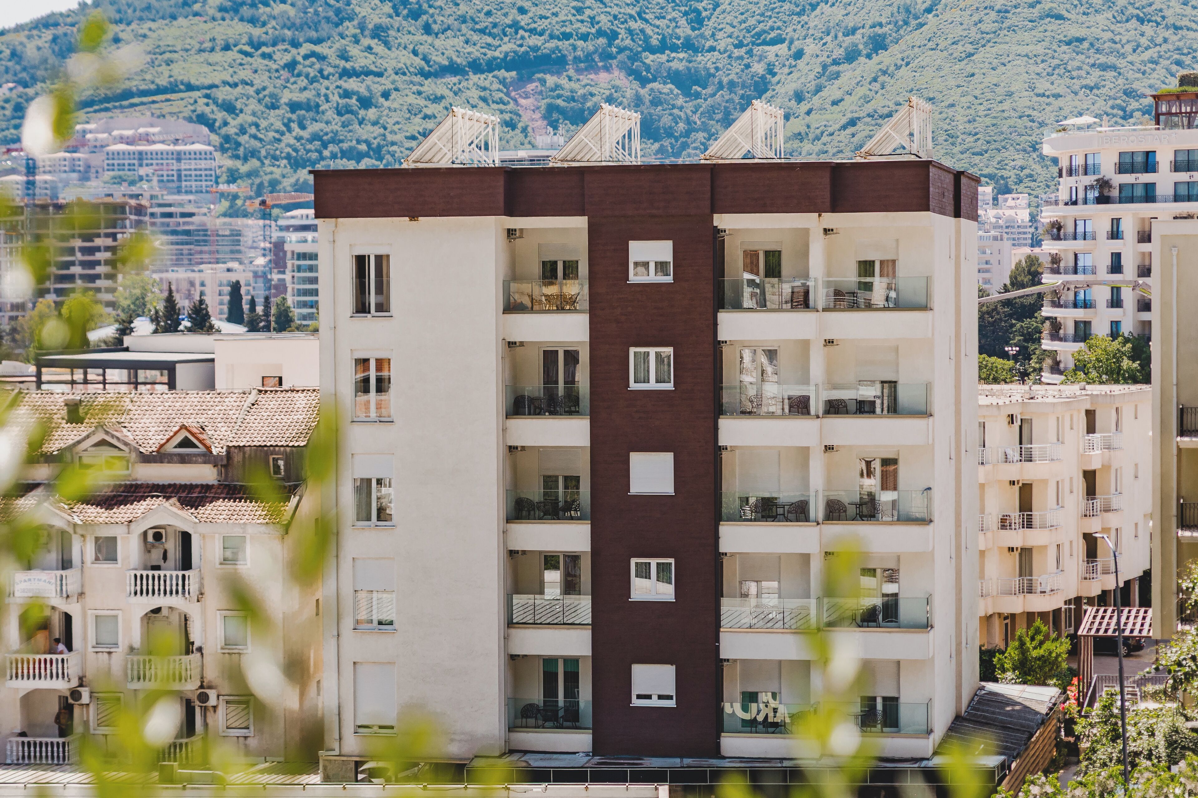 A multi-story building with balconies, a central brown section, and a view of a mountainous area in the background.