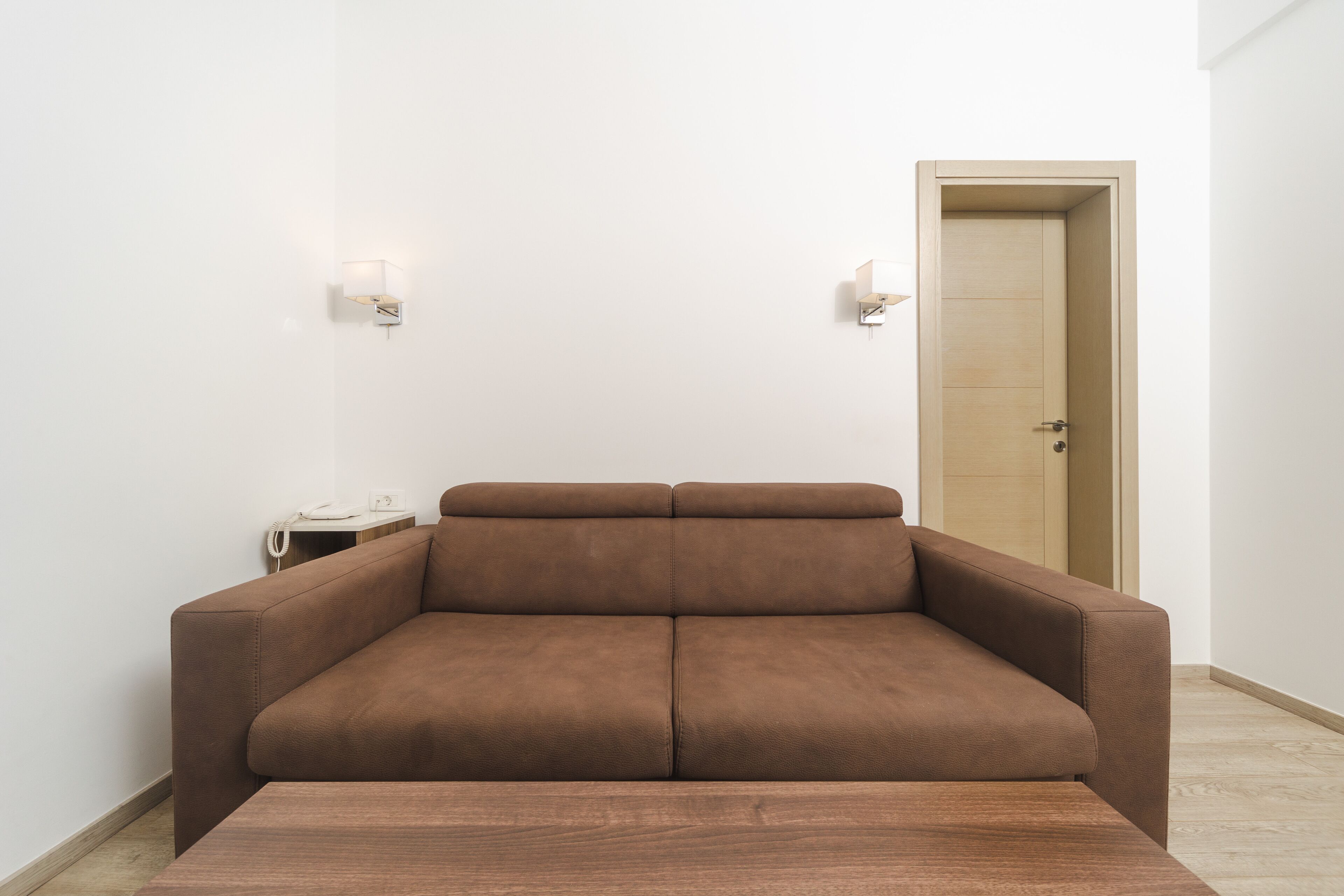 Ein braunes Sofa in einem Raum mit weißen Wänden und einer Holztür.
