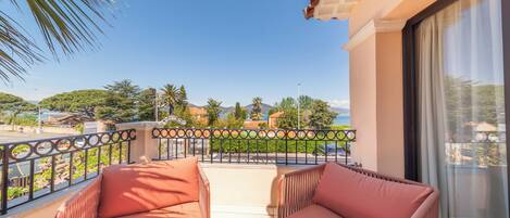 A balcony with two cushioned chairs, a railing, and a view of a coastal landscape with trees and buildings.