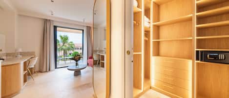 A modern hotel room with a large mirror, a wooden wardrobe, a dining area with a table and chairs, and a view of the outdoors.