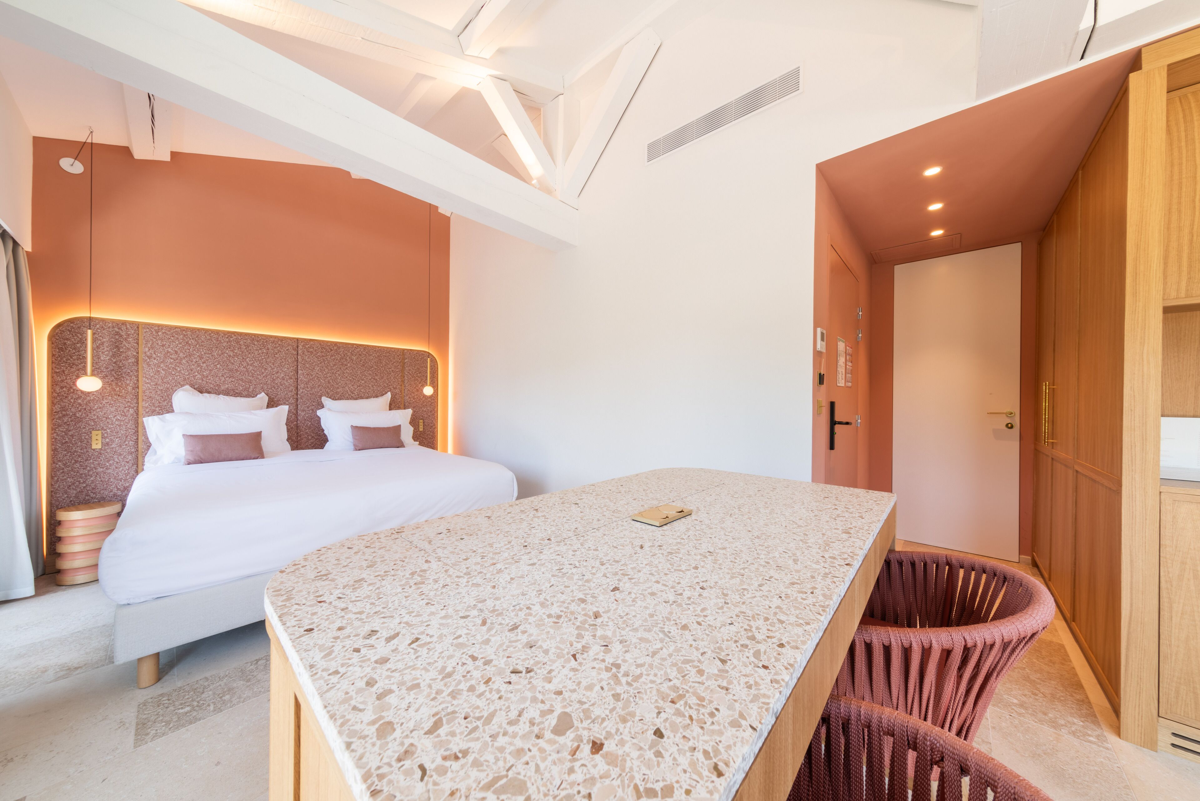 Quarto de hotel moderno com uma cama grande, uma mesa pequena e uma cadeira de vime.
